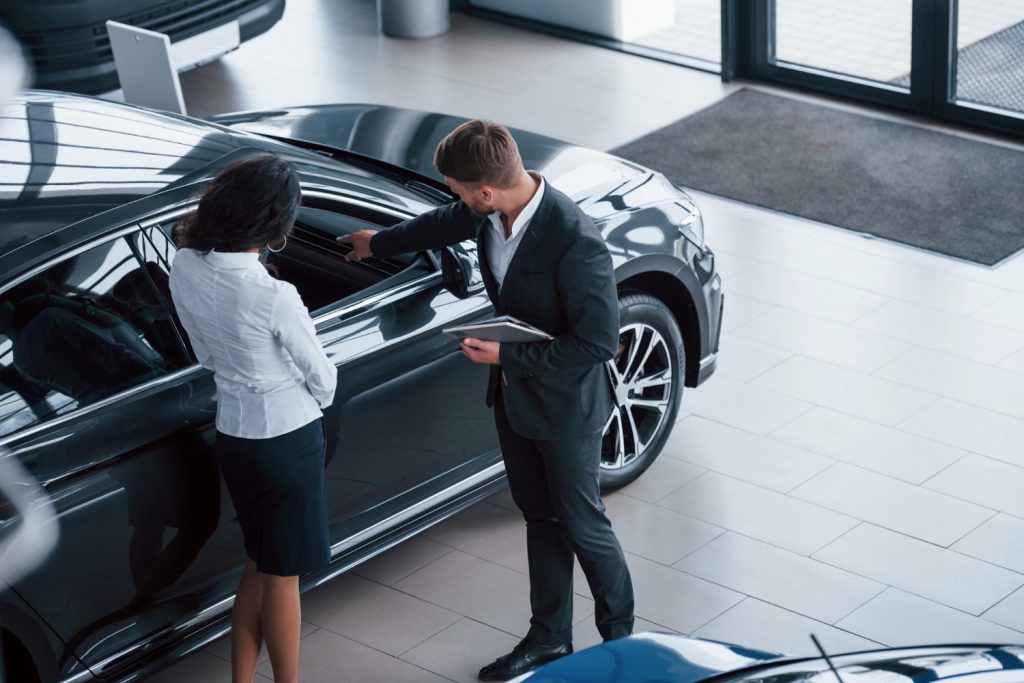 A man and woman examine a car together at a dealership, discussing features and options available for Booking.