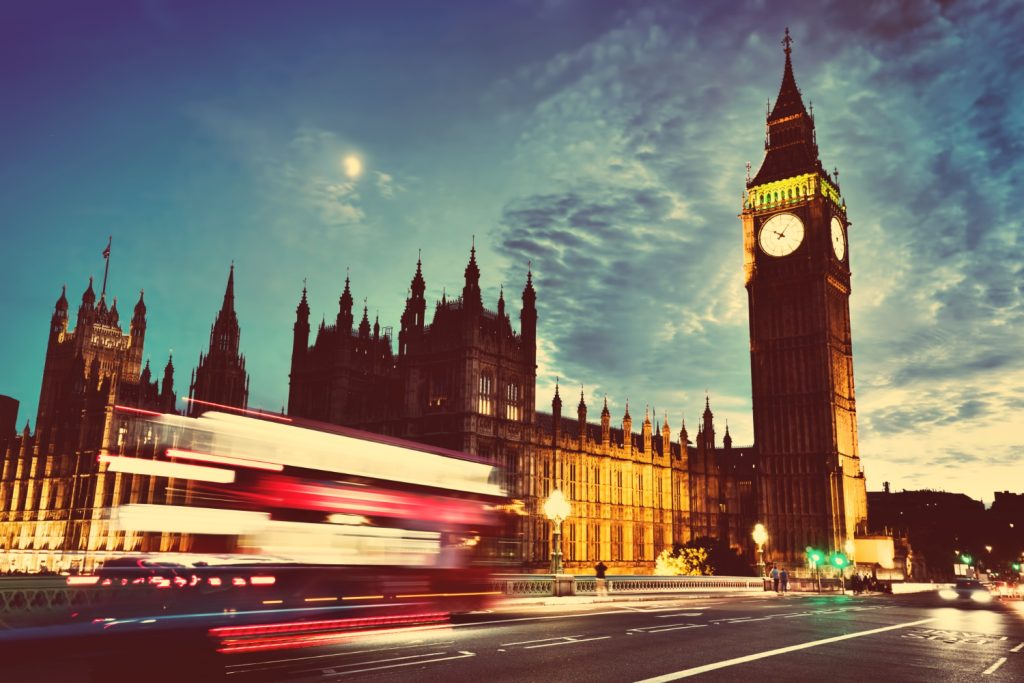 A bustling scene of London's Big Ben and the Houses of Parliament at twilight, with a red double-decker bus in motion.
