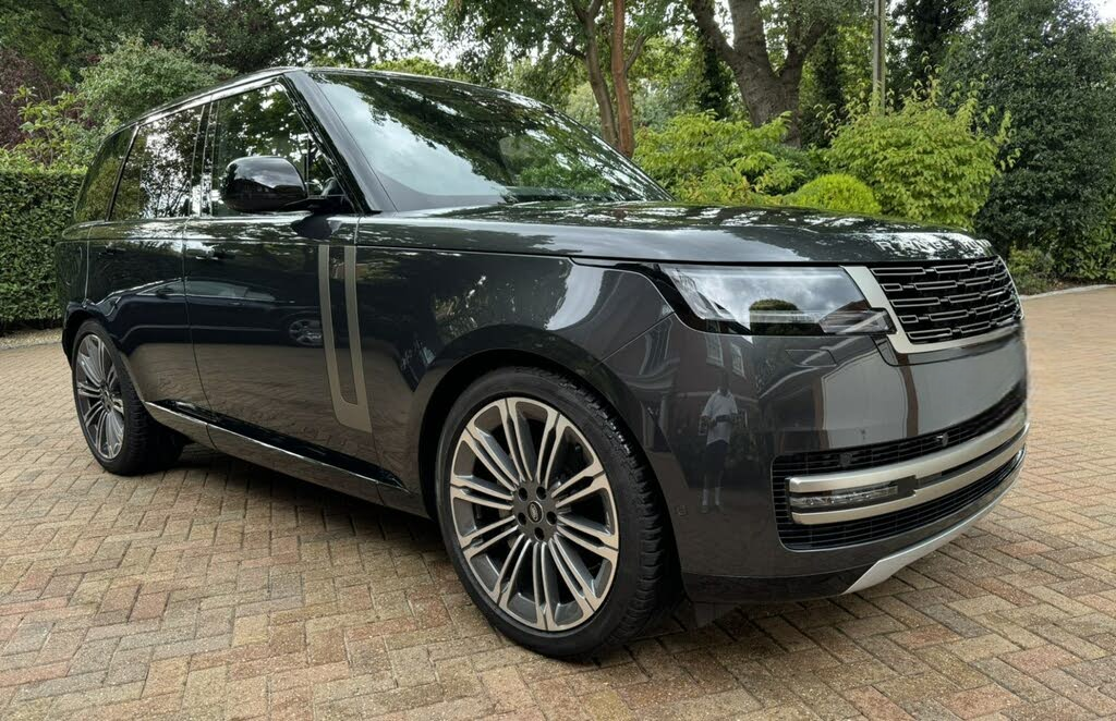 A sleek, dark gray luxury SUV parked on a patterned driveway with lush greenery in the background.